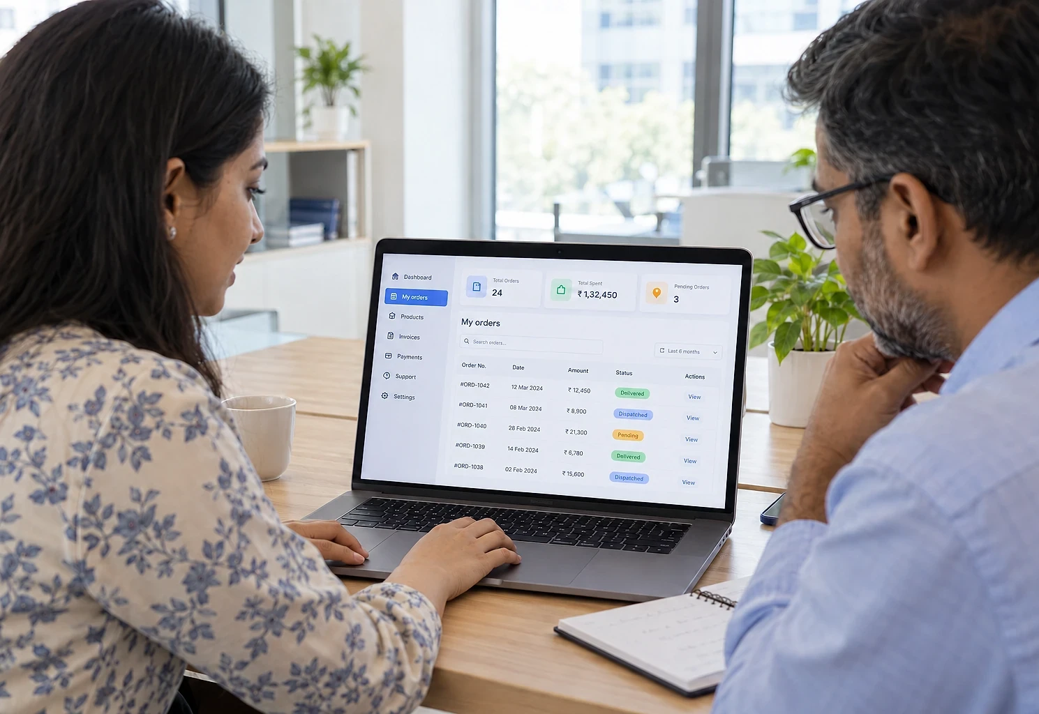 Two colleagues reviewing a customer's orders and statuses in a business portal on a laptop