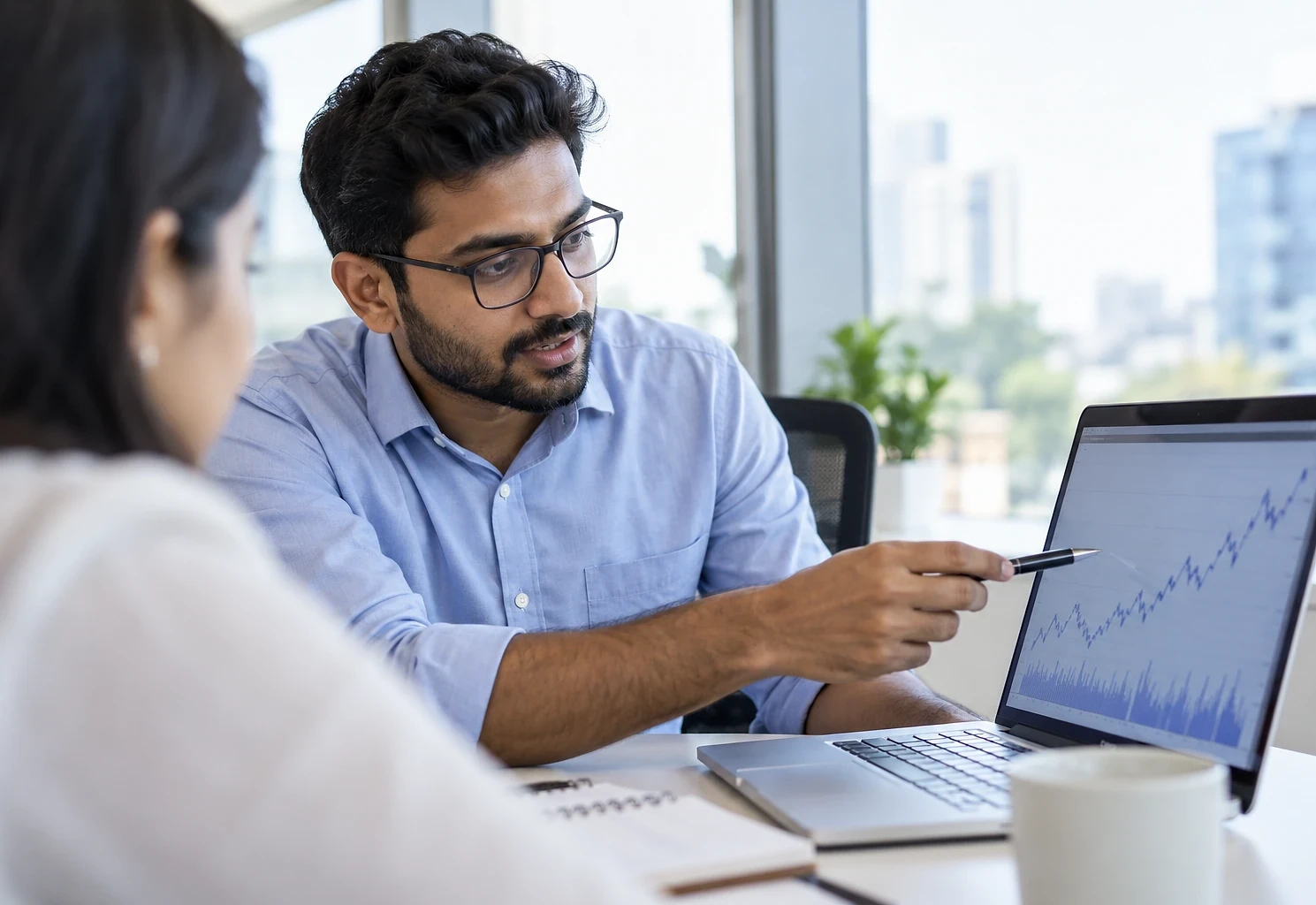 Analyst pointing at a trend chart on a laptop for a colleague